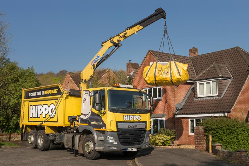 HIPPO truck lifting a HIPPOBAG from the driveway of a house