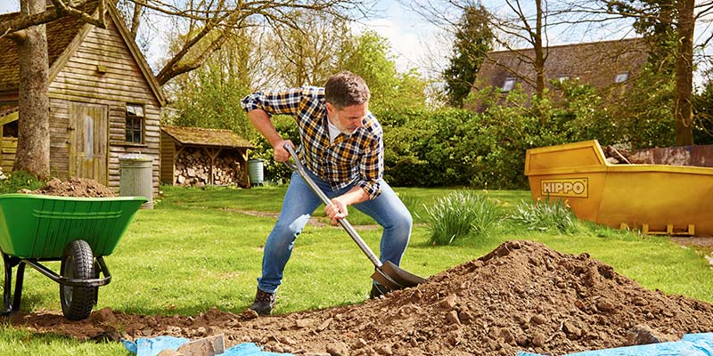 Man putting soil into a wheelbarrow to put in a skip