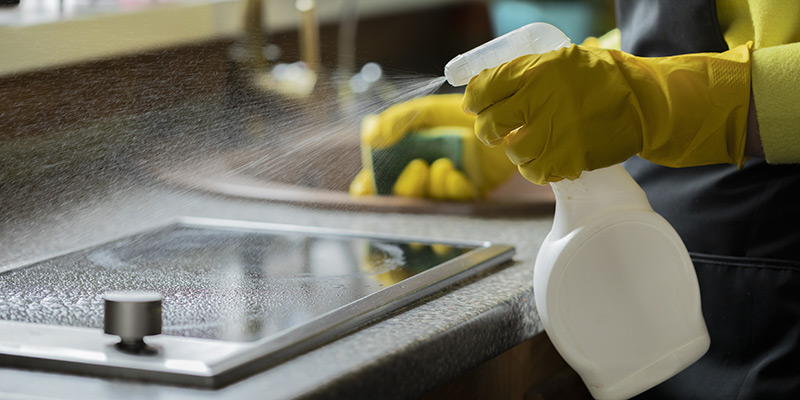 Person cleaning kitchen with cleaning spray and yellow rubber gloves
