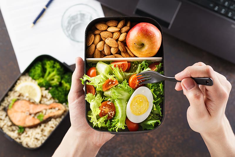 A fresh packed lunch ready to eat held over a work desk with a laptop and paper