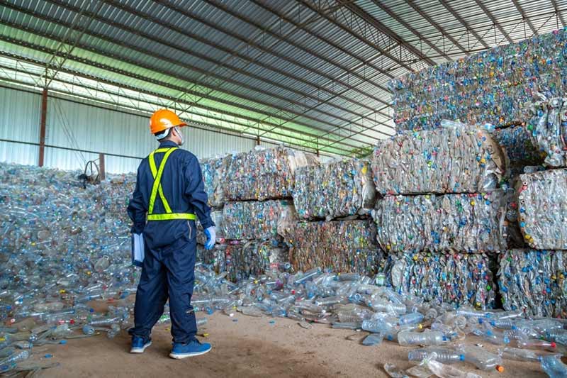 Man standing in front of bundled plastic waste in a recycling storage unit