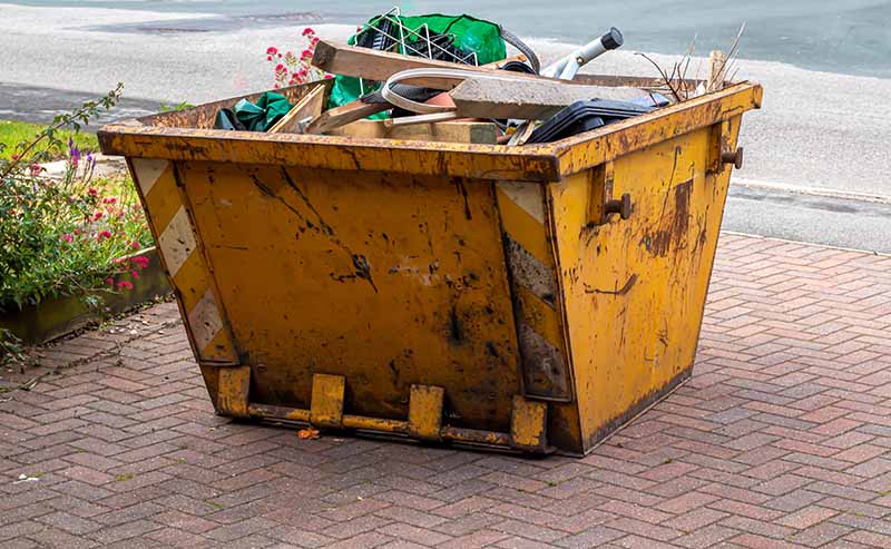 Yellow skip on a driveway filled with rubbish