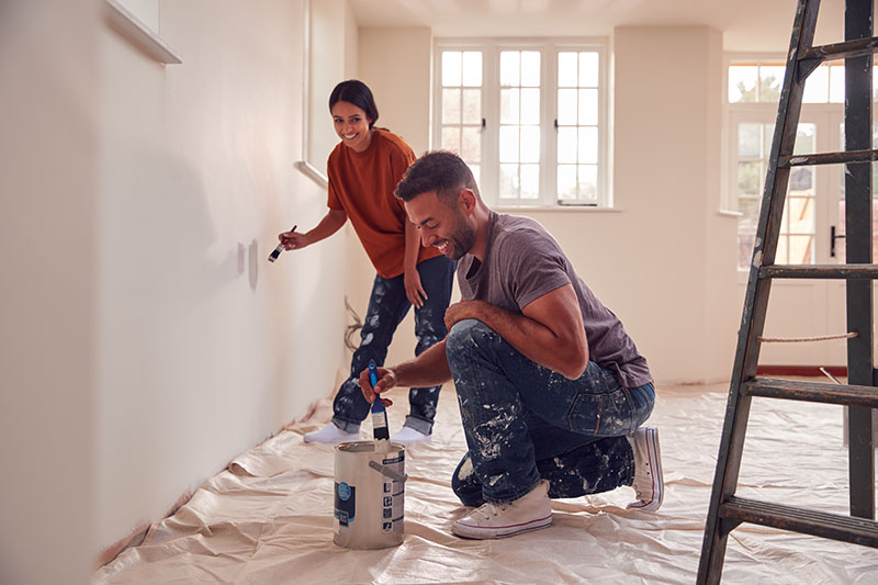 Couple painting a room with protective floor coverings and a step ladder
