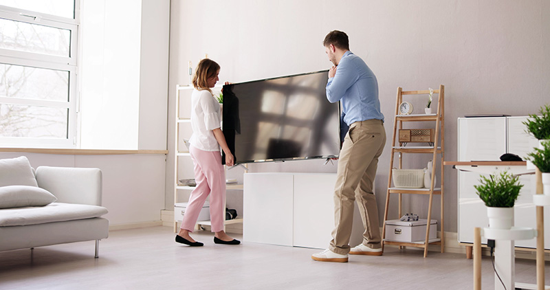 Couple carrying a TV to place on a side unit in a living room