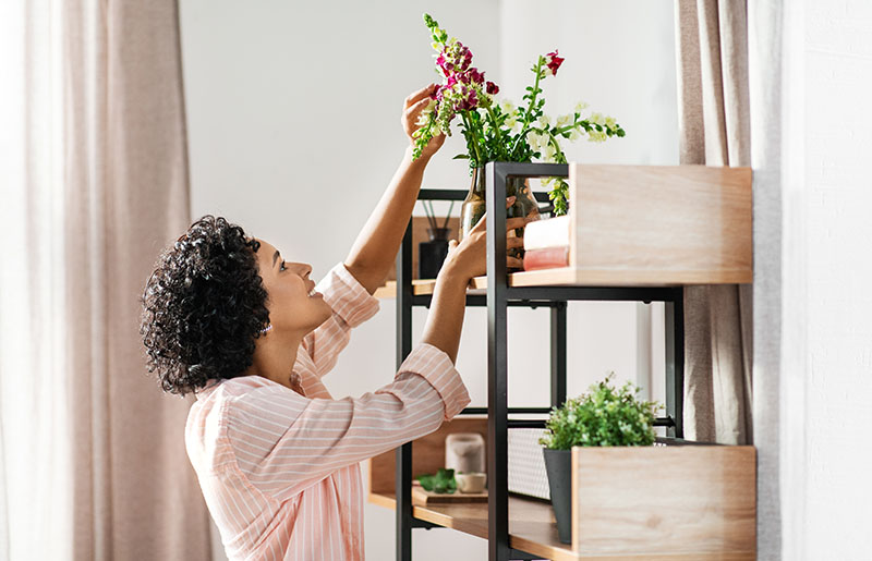 Woman placing flowers on wall shelves in a home
