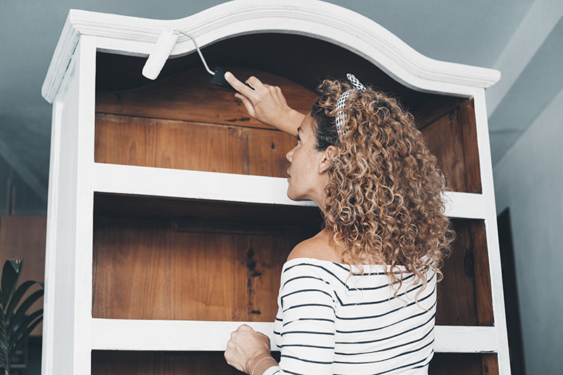Woman painting a wooden bookcase for upcycling