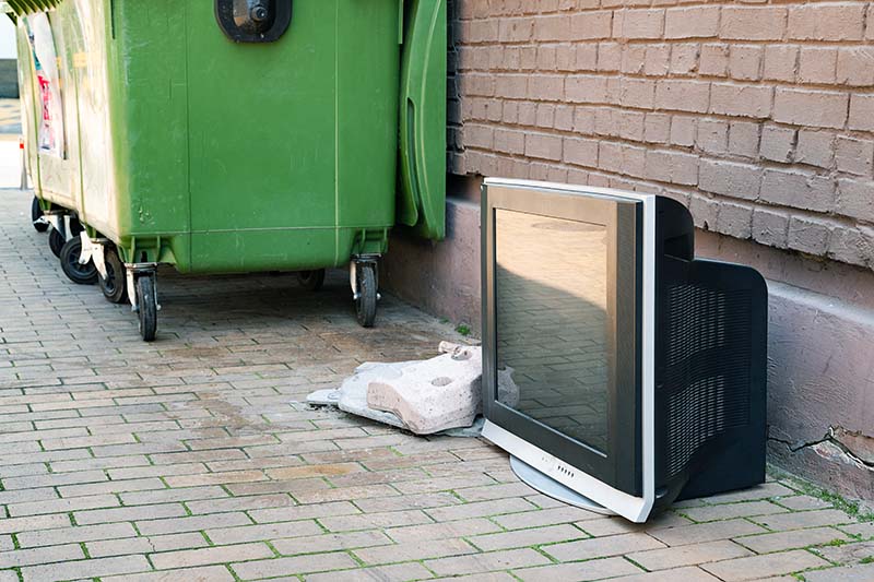 An old TV illegally dumped by waste bins