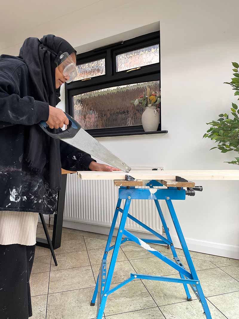 Woman sawing wood to build floating shelves DIY project