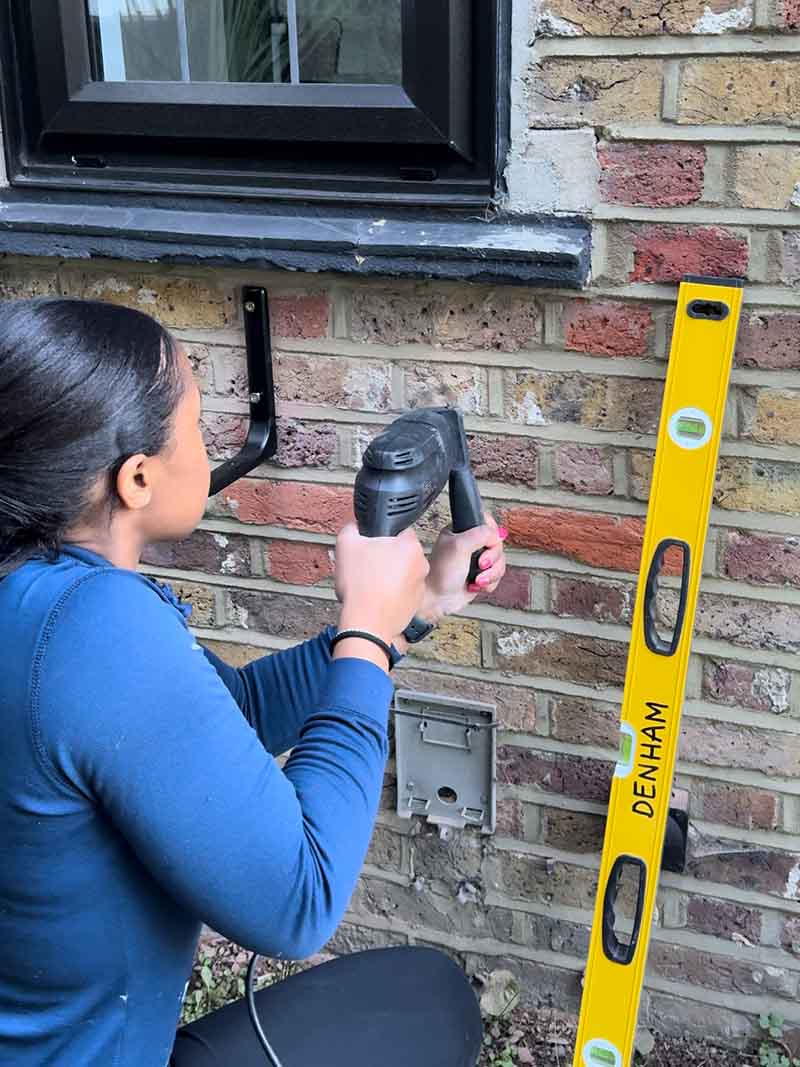 Woman drilling hole in an exterior brick wall for brackets