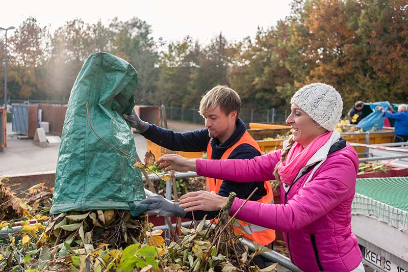 Woman and man emptying green waste into a skip at a recycling centre