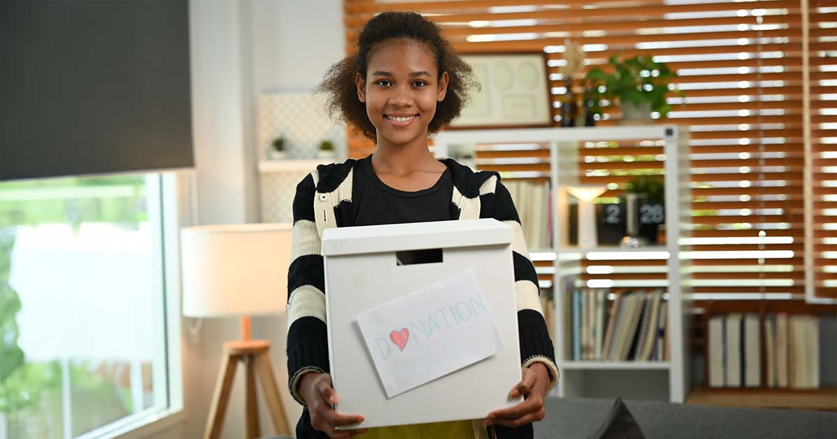 Lady holding a box with a handwritten donation note stuck on it in a living room space