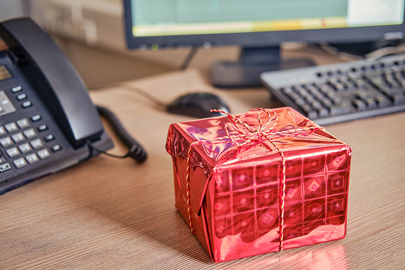 Christmas gift in red shiny wrapping paper with a bow placed on a work desk