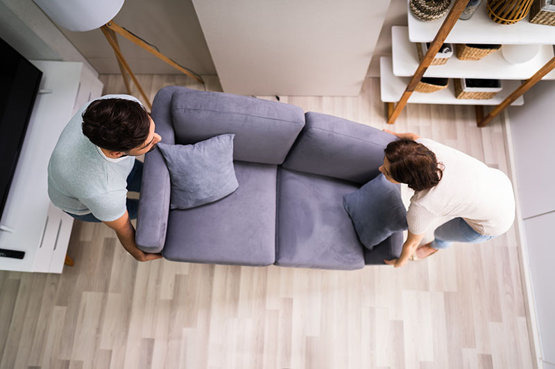 A couple lifting a two seater sofa in a living room