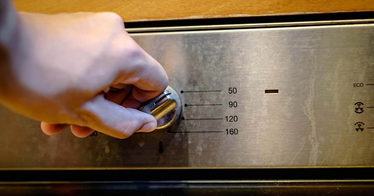 A hand turning the temperature dial on an old oven